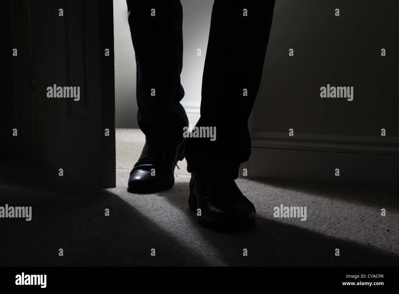 Male wearing black shoes entering a dark room, back lit. Close up sinister evil Stock Photo