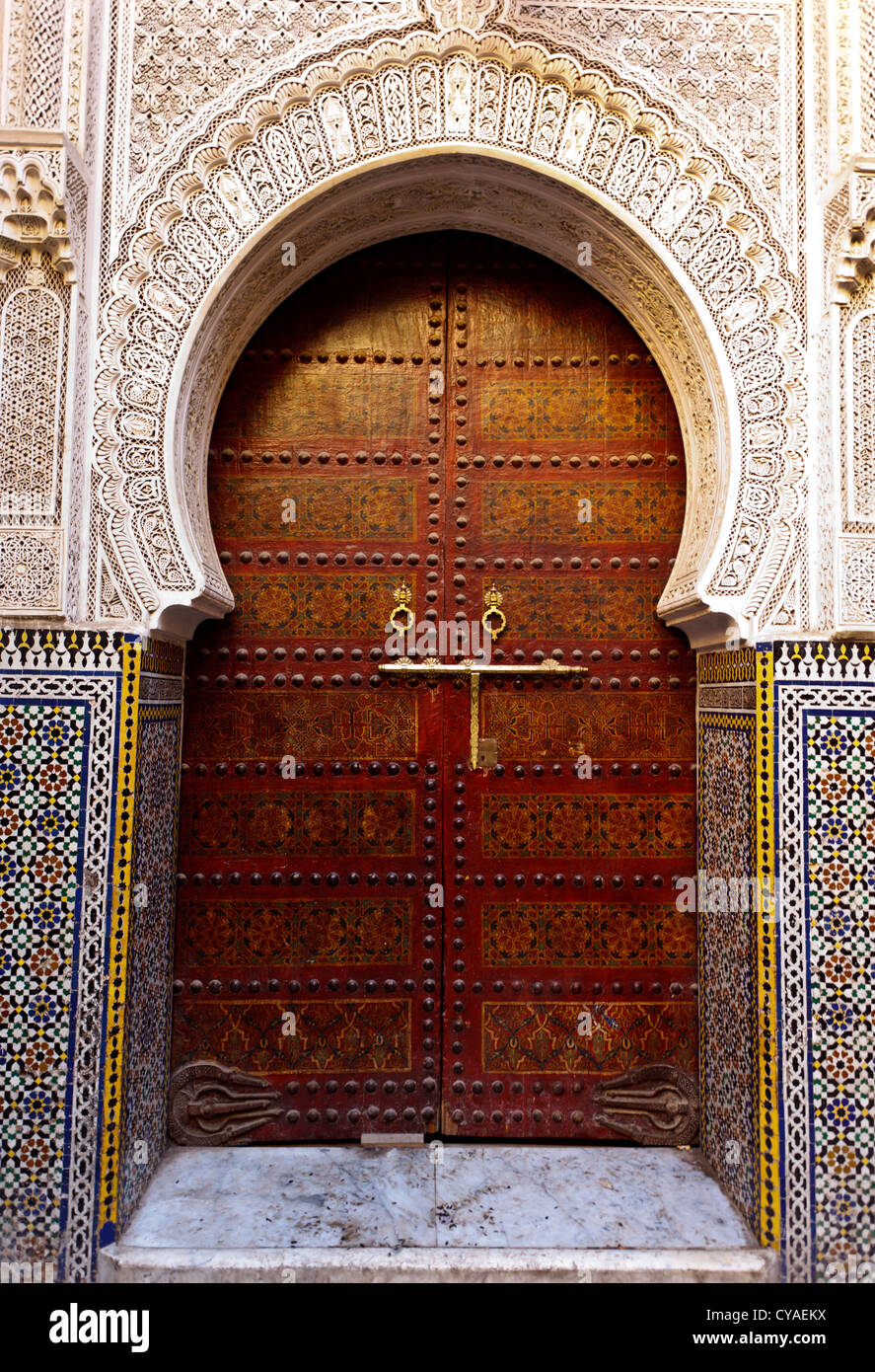 Ornate exterior brass door surrounded by arch decorated with mosaic tile of historic Moorish style building in Fez, Morocco Stock Photo