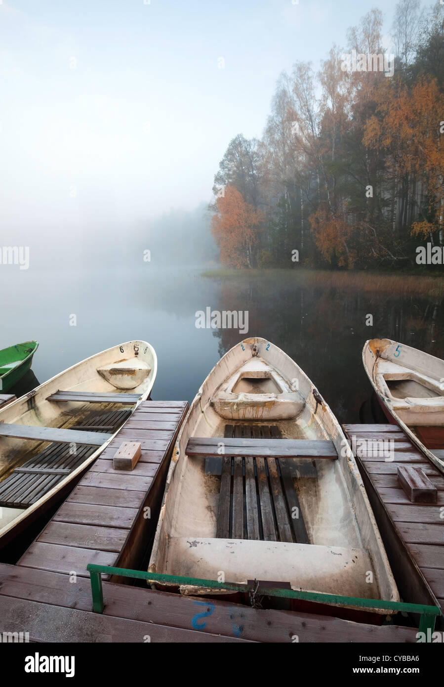 Late autumn foggy morning. Small wooden pier with rowboats on still lake Stock Photo