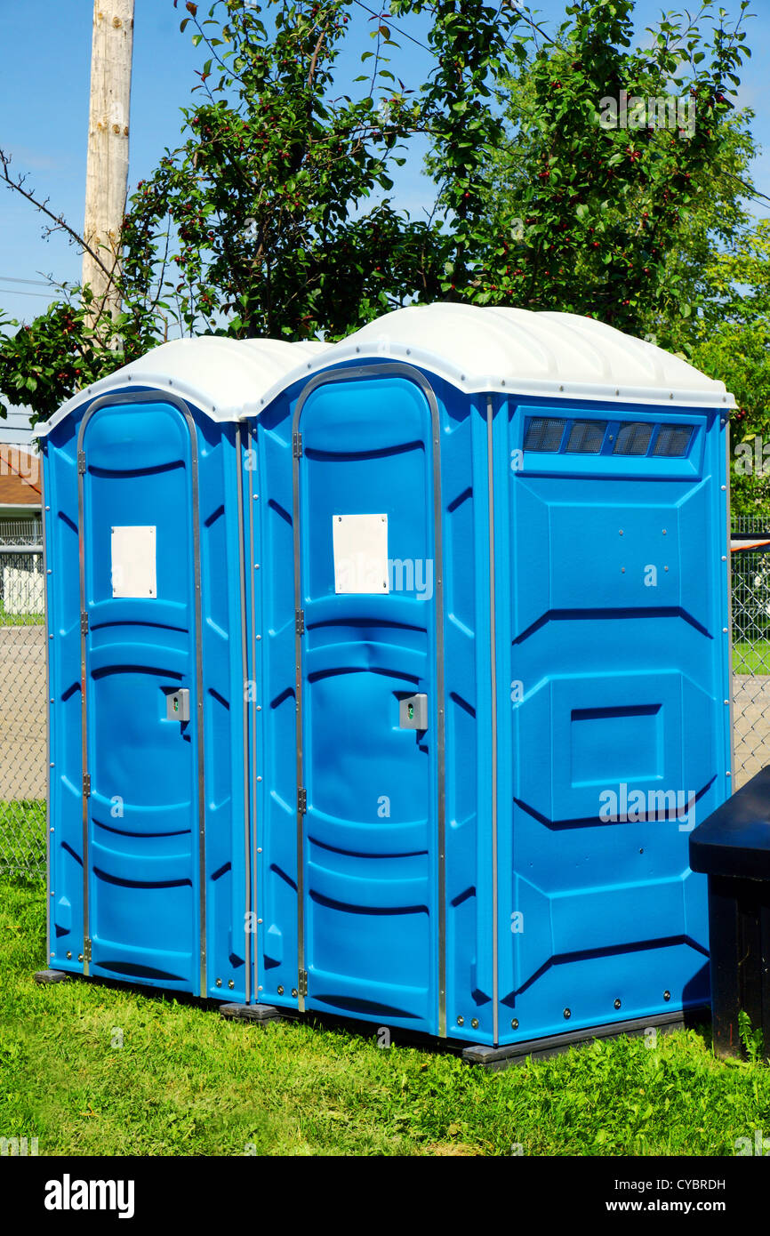 Two portable toilet or loo in blue plastic at a park public event or concert, with white sign on door ready for text. Stock Photo