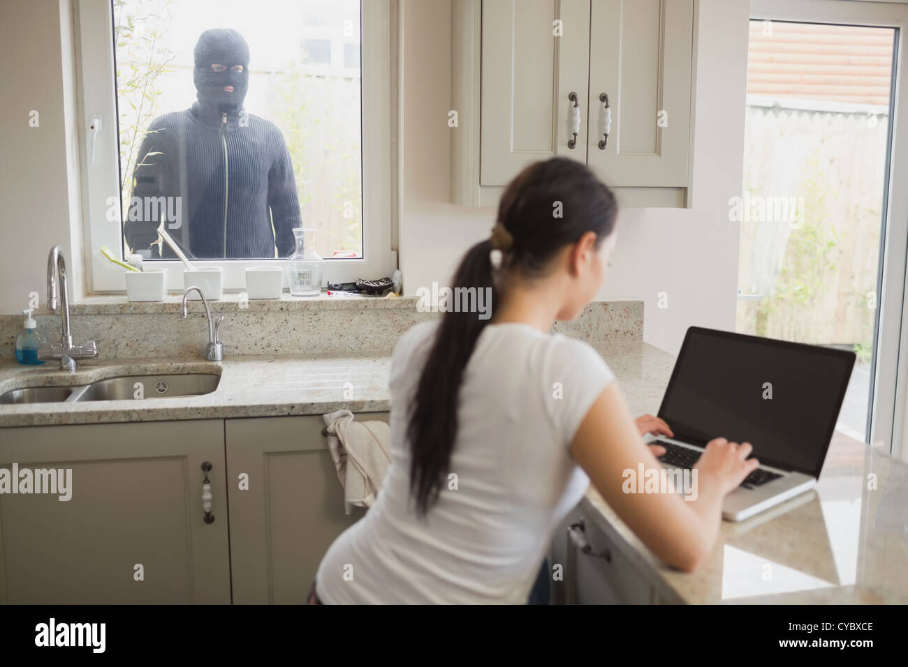 Woman being observed by burglar through window Stock Photo