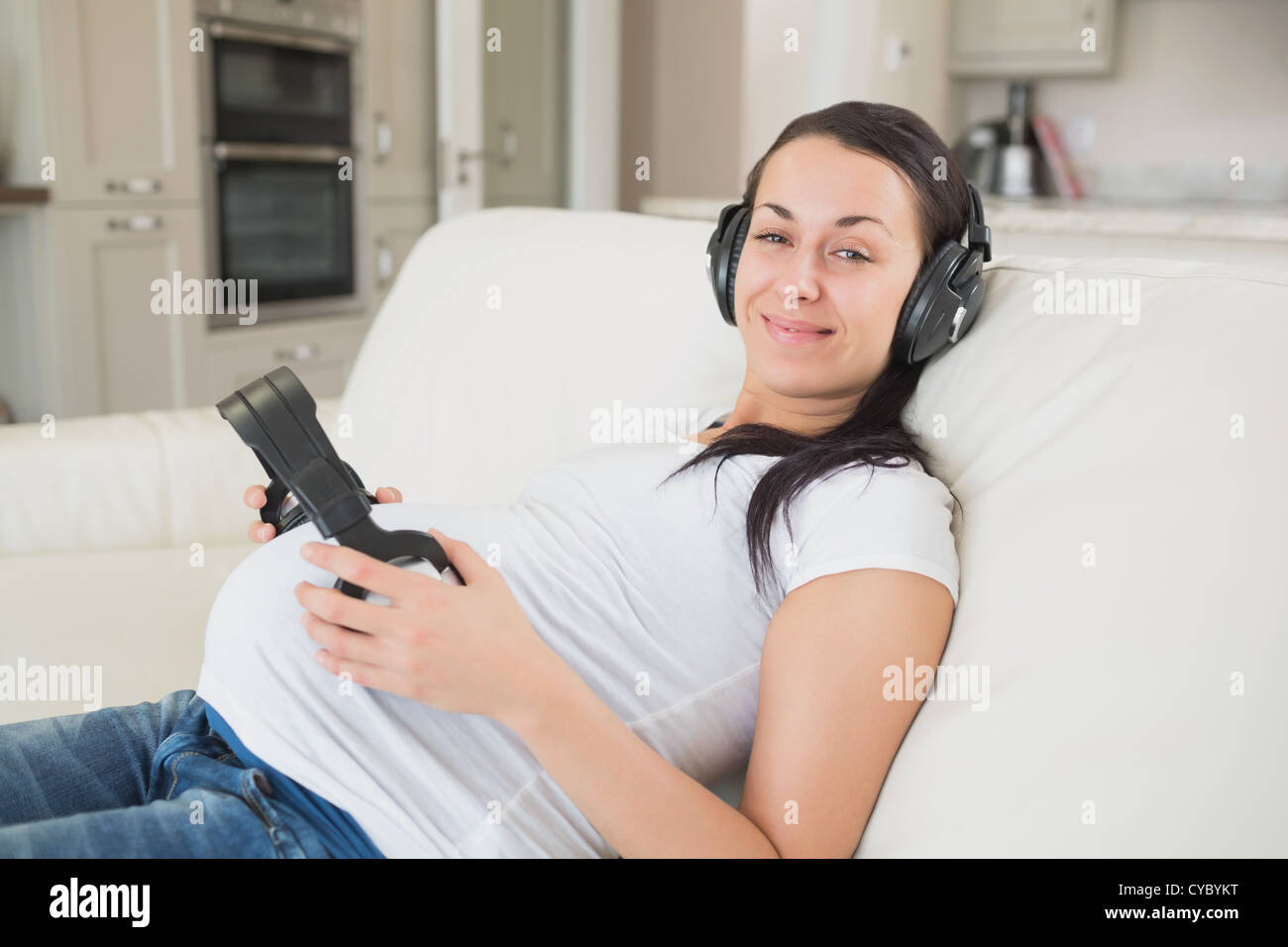 Prospective mother lying on the couch listening to music and holding headphones to belly Stock Photo