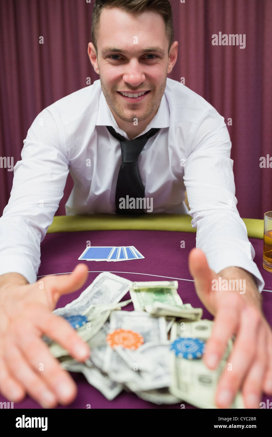 Happy man at poker table taking his winnings Stock Photo