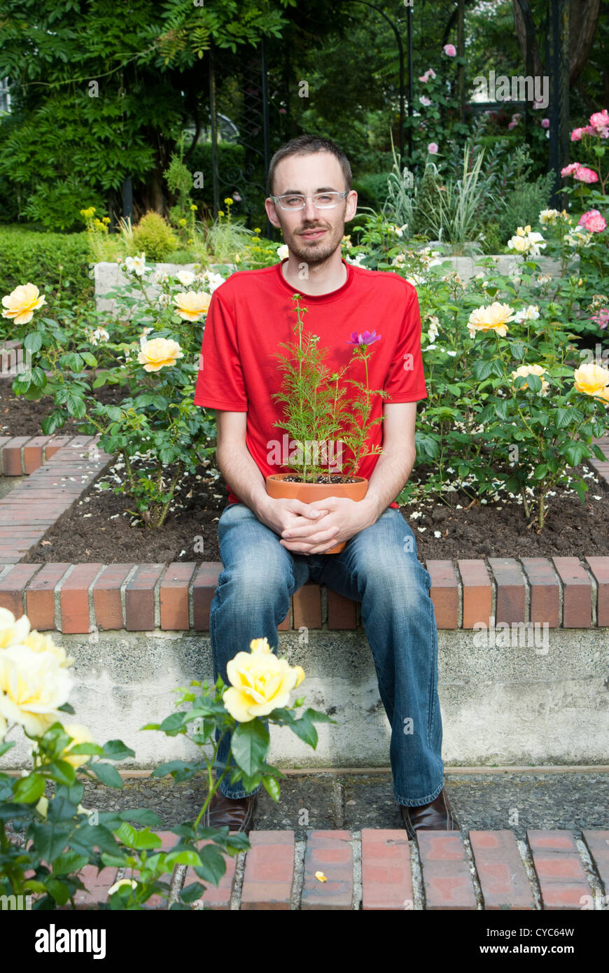 Man sitting on a bench in a garden holding a potted plant Stock Photo ...