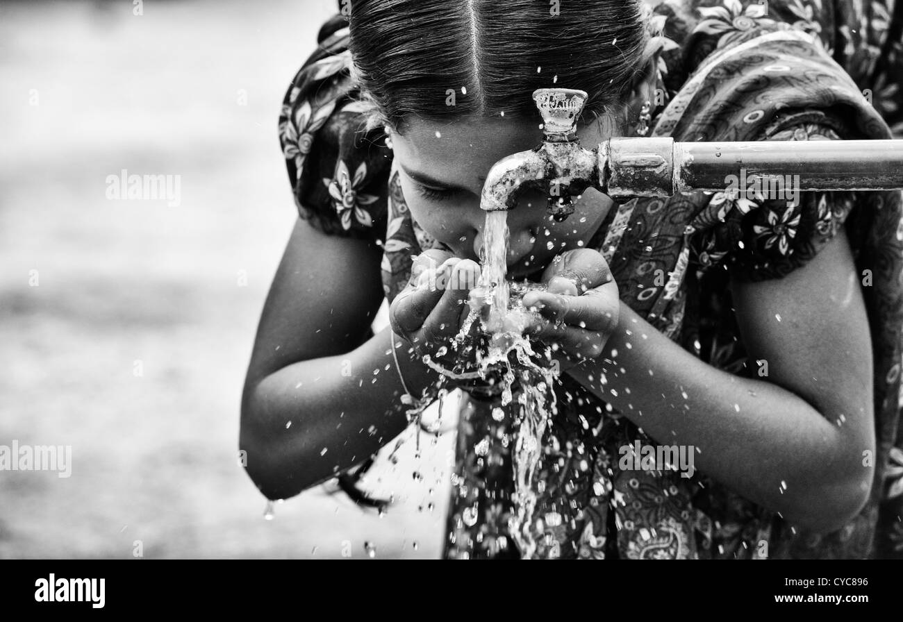 Indian girl drinking from a communal water tap in rural indian village. Andhra Pradesh, India. Monochrome Stock Photo