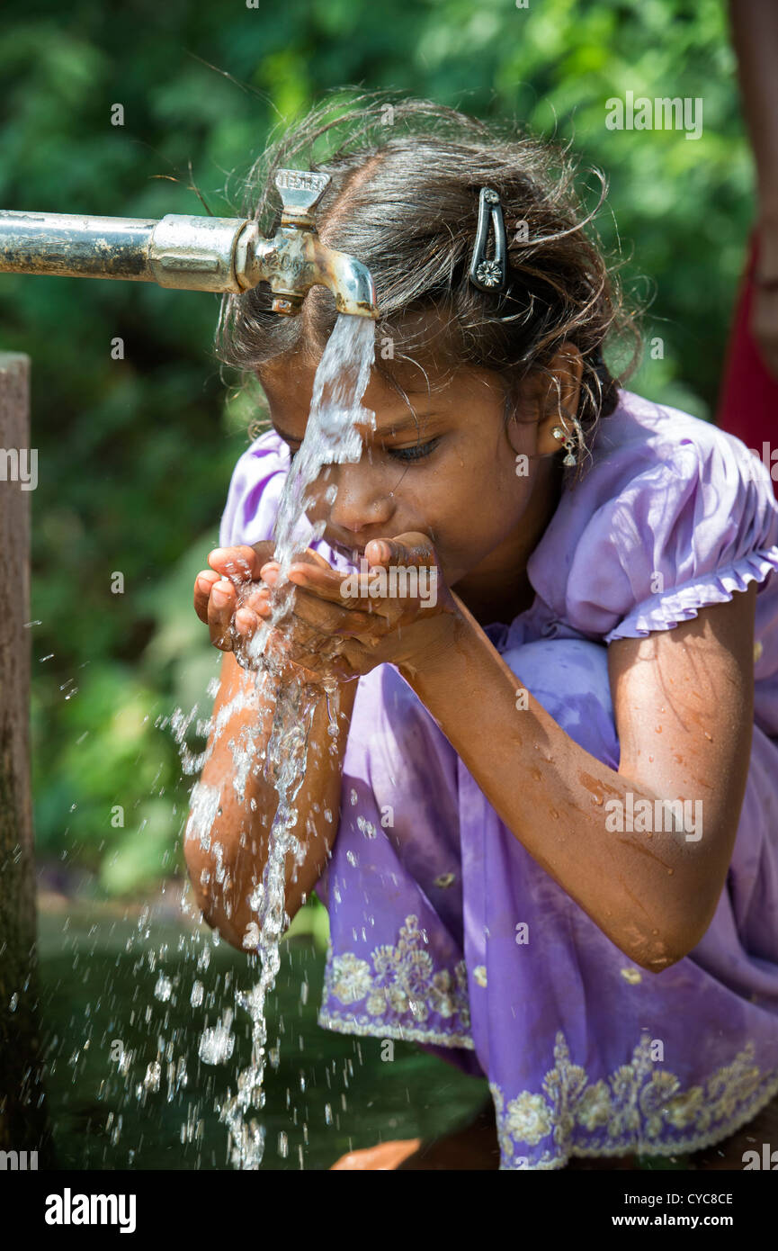 Indian girl drinking from a communal water tap in rural indian village
