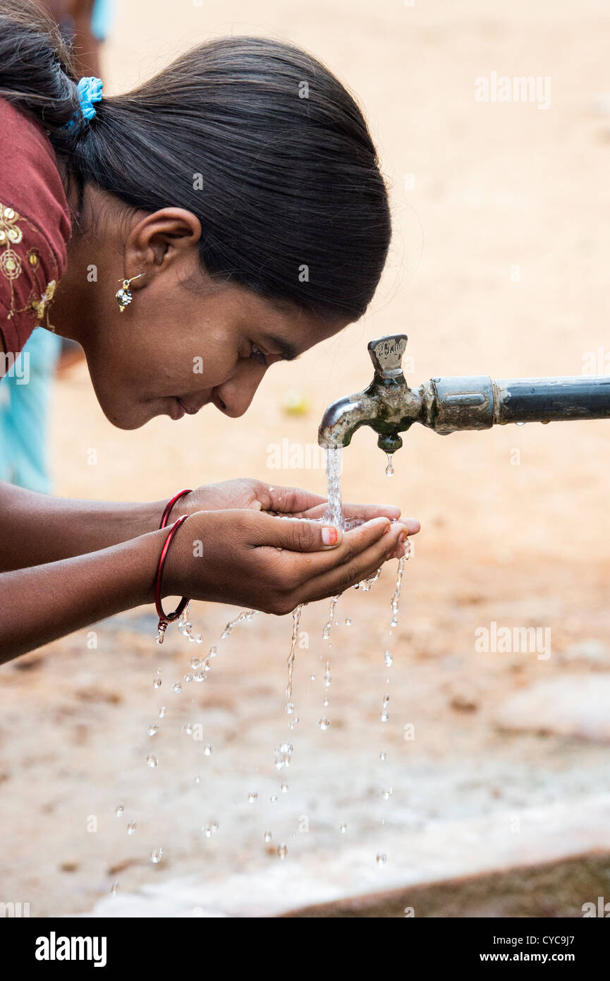 Indian girl drinking from a communal water tap in rural indian village