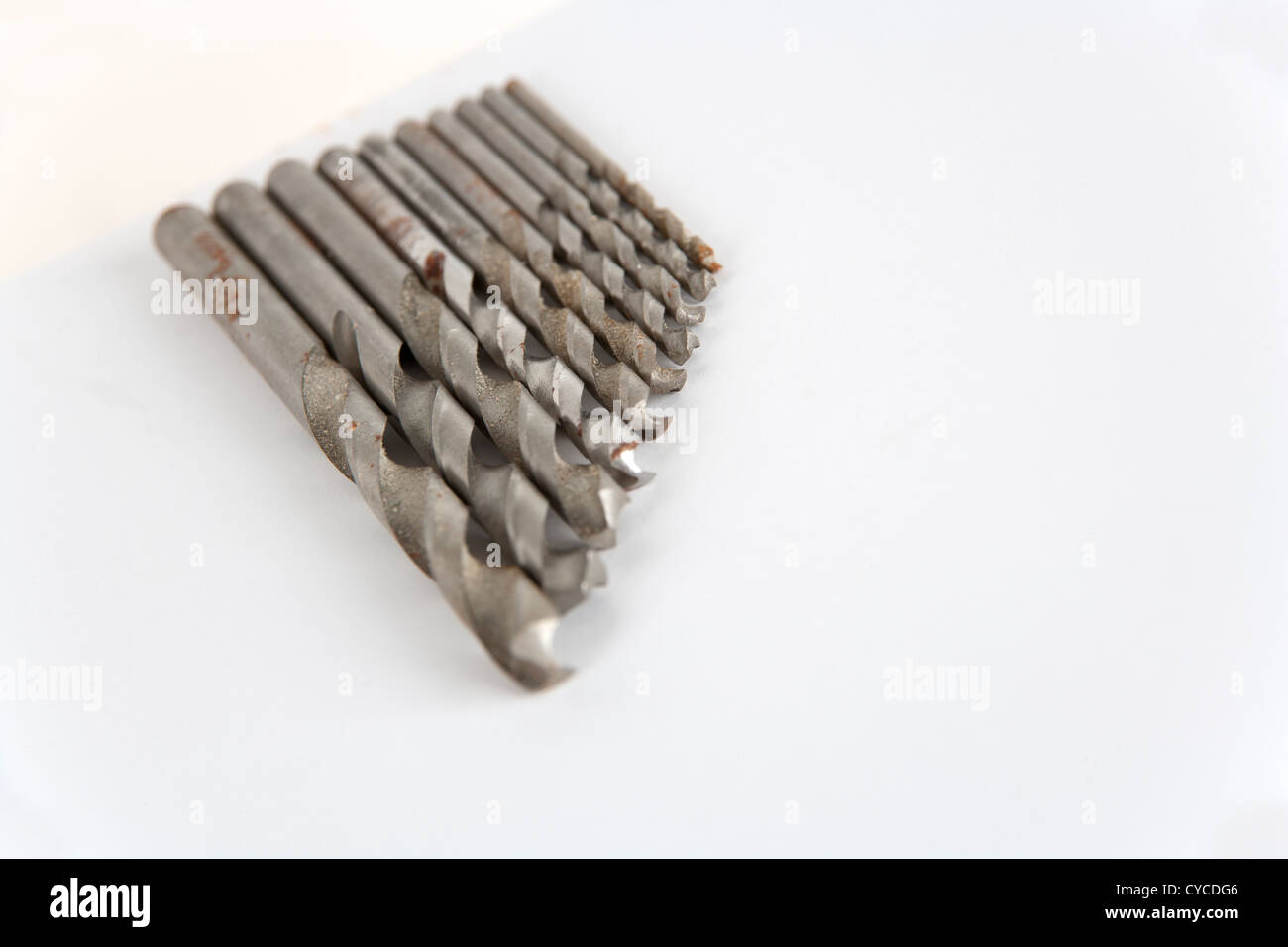 Well used and rust specked twist drill bits on white paper with copy space. Shallow depth of field. Stock Photo