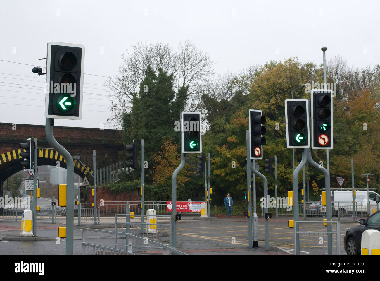 Complex set of traffic lights and pedestrian crossing lights with rail bridge in background with lights on green / left turn Stock Photo