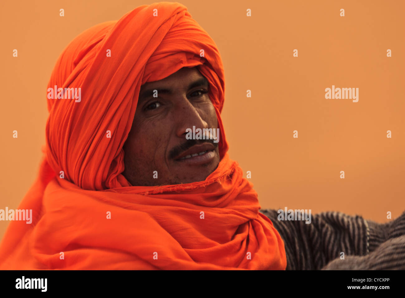 Portrait of Berber man in the Sahara with orange turban head garb blowing in the wind in Merzouga, Morocco. Stock Photo