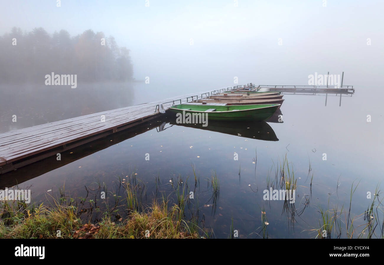 Small wooden pier with boats on lake in cold foggy morning Stock Photo
