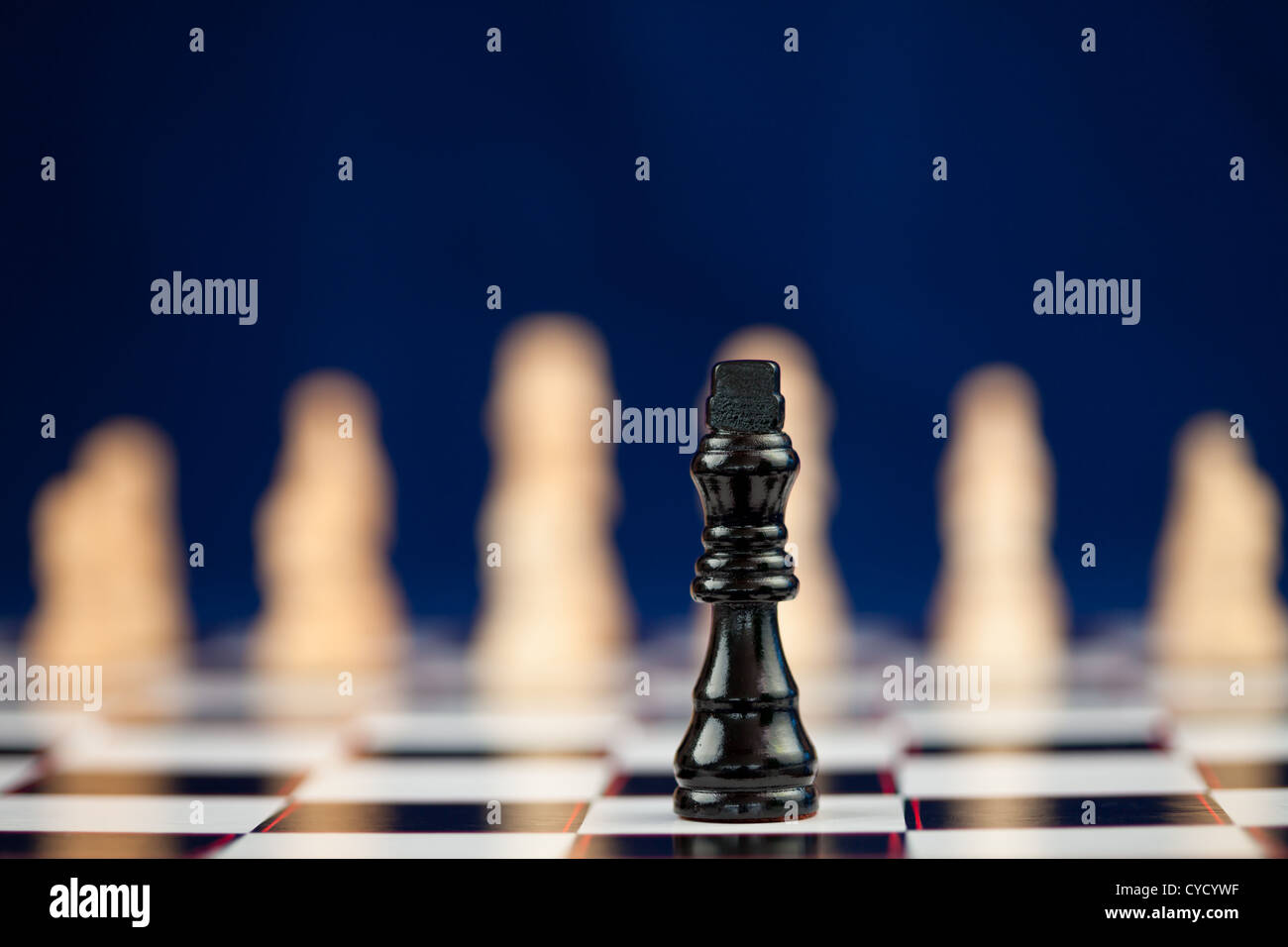 Black chess piece standing at the chessboard white ones behind Stock Photo