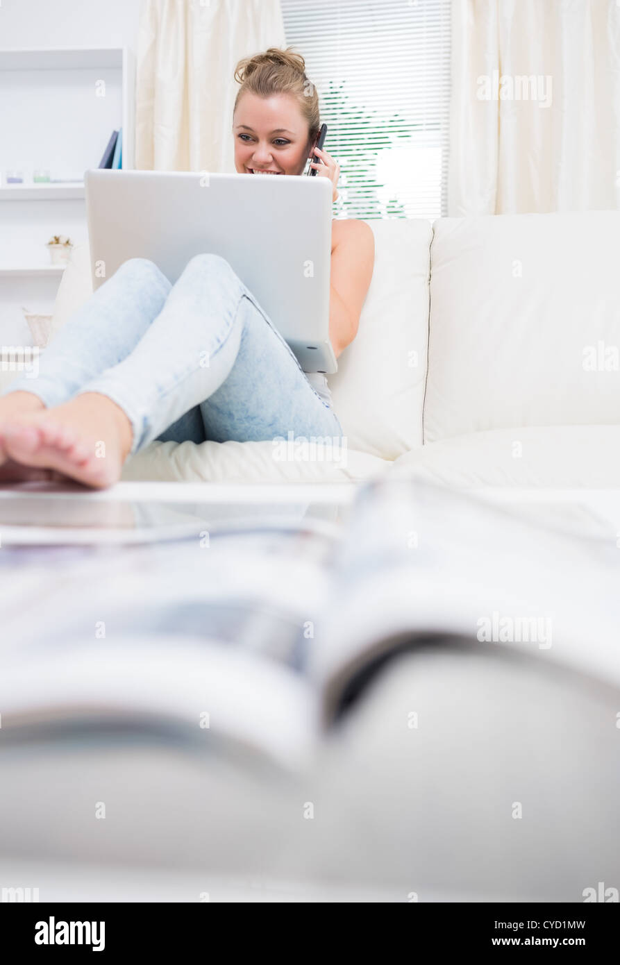 Woman sitting on the couch while using laptop and calling Stock Photo ...
