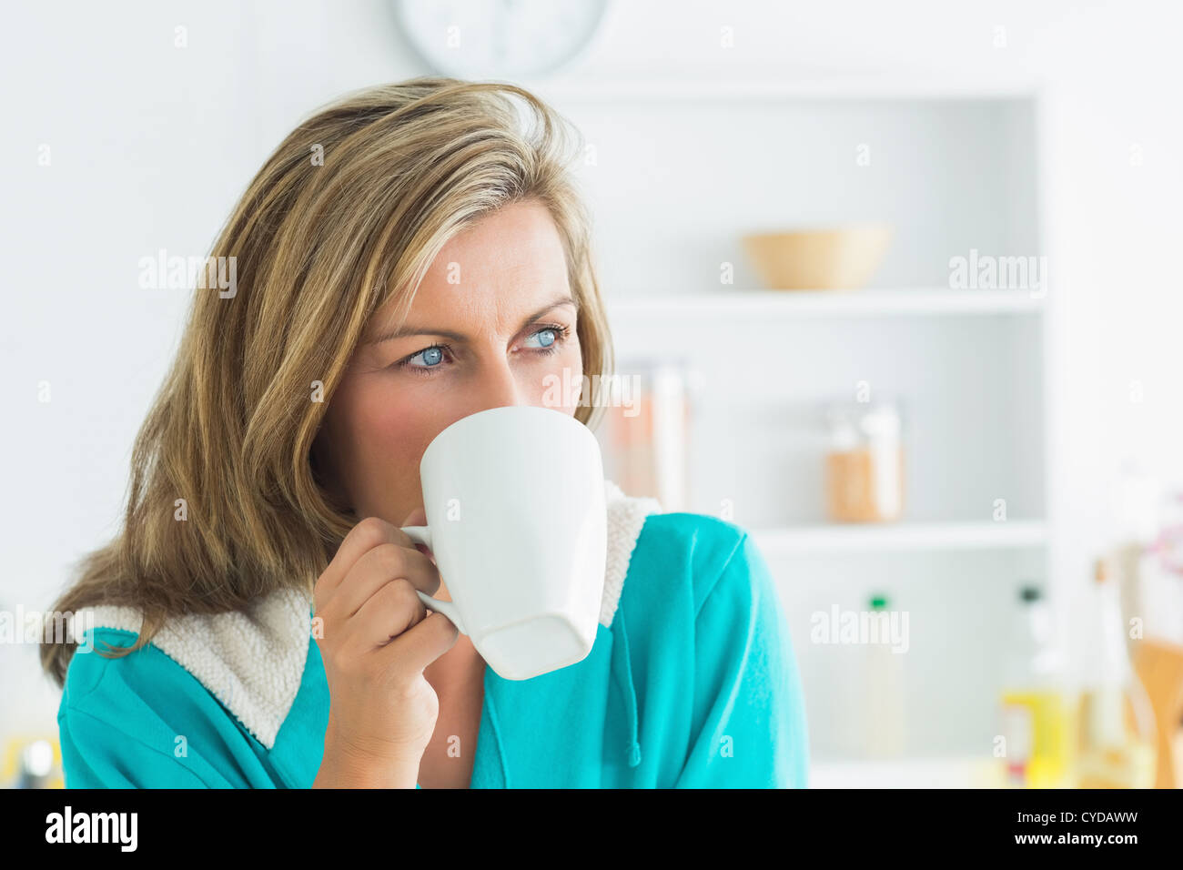 Woman in dressing gown sitting in the kitchen and drinking Stock Photo