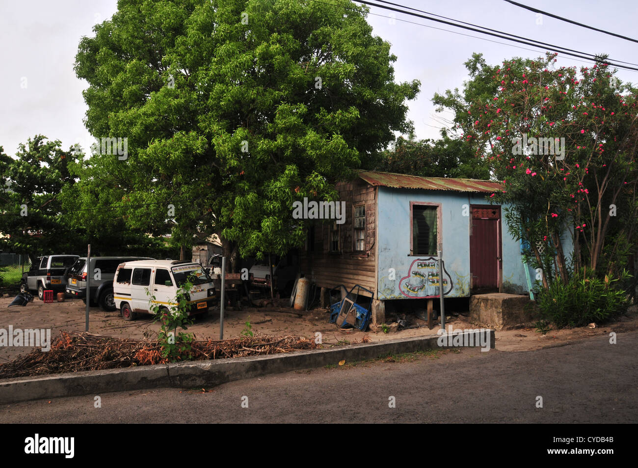 Cars parked earth yard by small blue wooden house, 'Bonga's Blue Studio', Belair Road, Hillsborough, Carriacou, West Indies Stock Photo