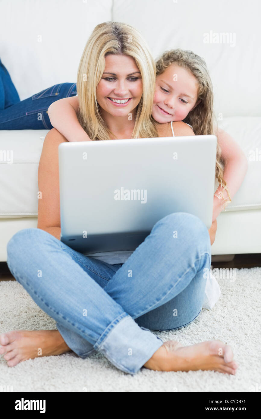 Mother sitting on the floor while her daughter hugging her from the sofa Stock Photo
