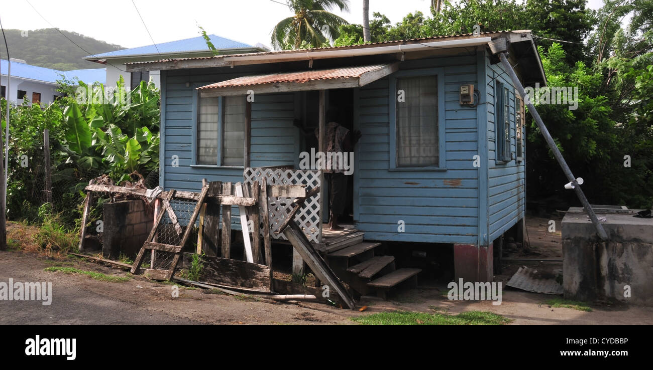 Morning sun view man standing porch small blue painted wooden planks house, Belair Road, Hillsborough, Carriacou, West Indies Stock Photo