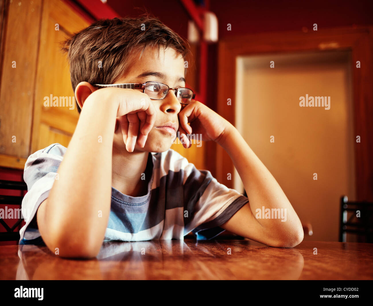 Contemplation: boy sits at table. Stock Photo