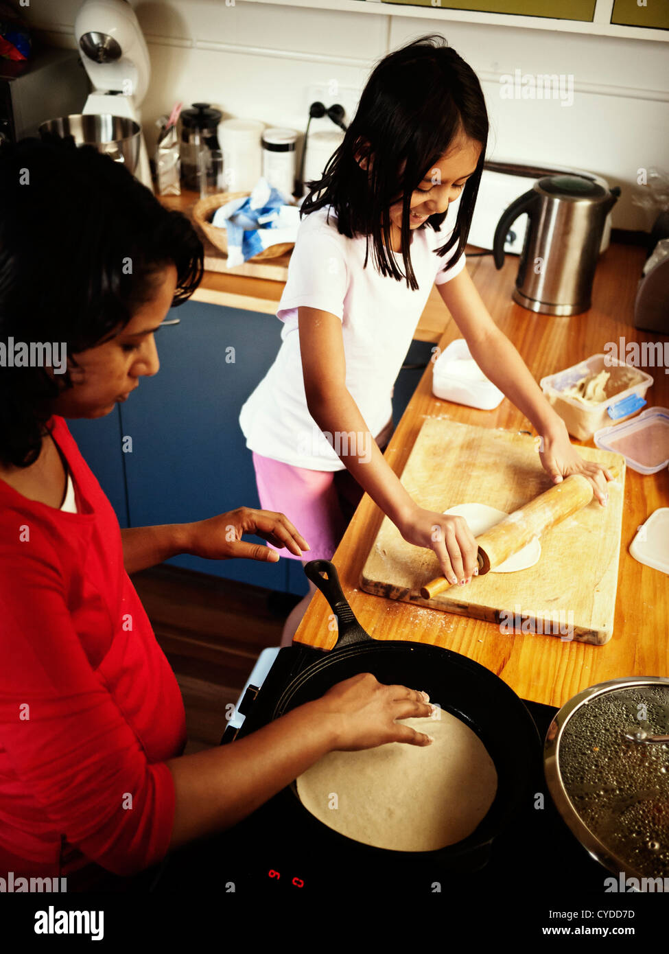 Girl helps her mother with cooking by rolling out chapatis Stock Photo