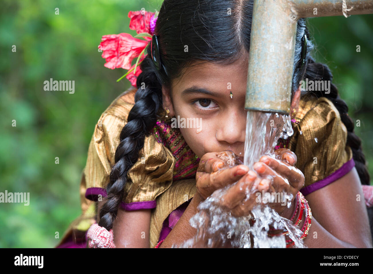 Young Indian girl drinking from a hand water pump in a rural indian