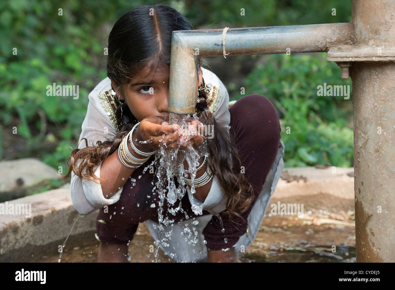 Young Indian girl drinking from a hand water pump in a rural indian village. Andhra Pradesh, India Stock Photo