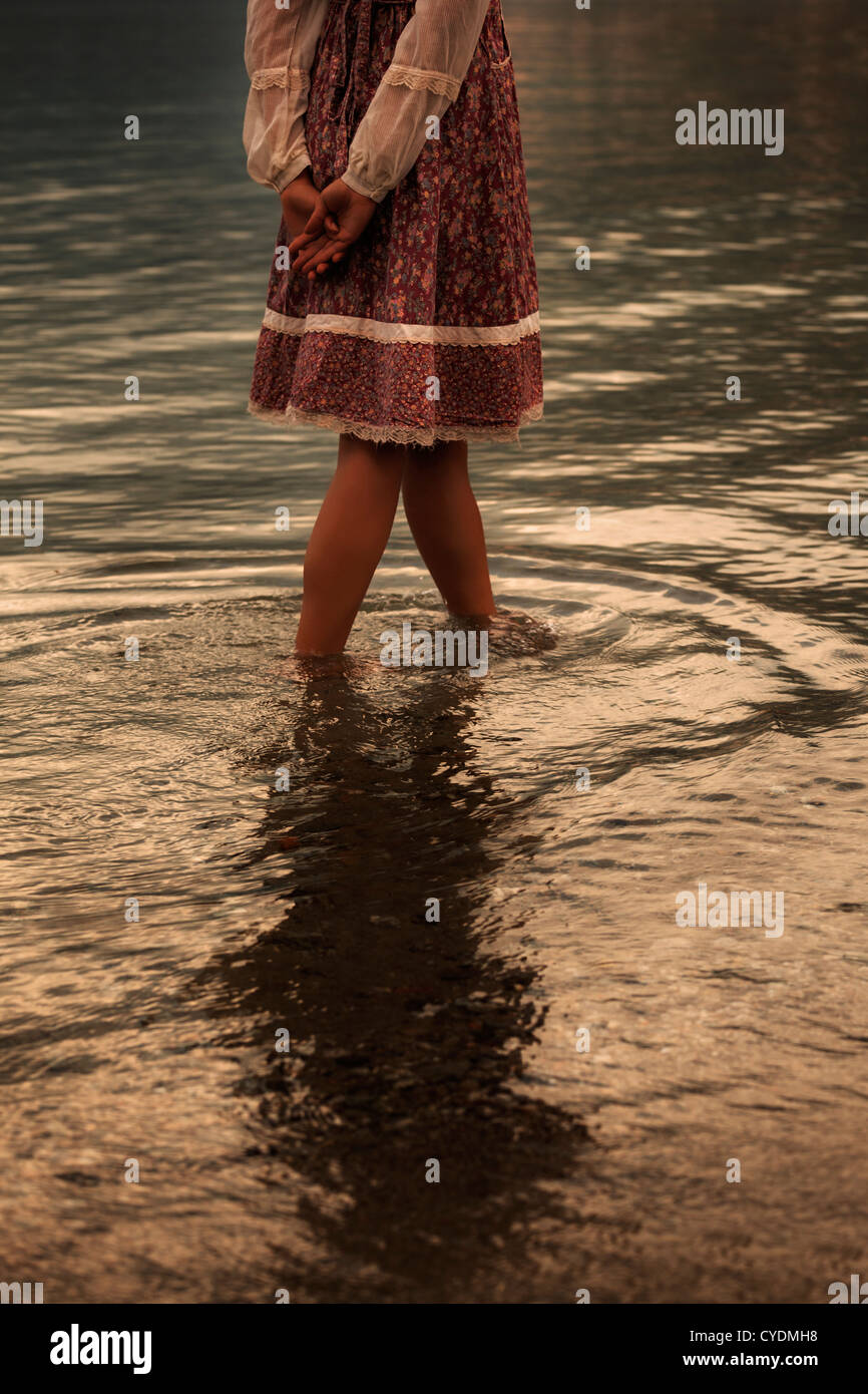 a girl in a vintage dress is walking in water Stock Photo