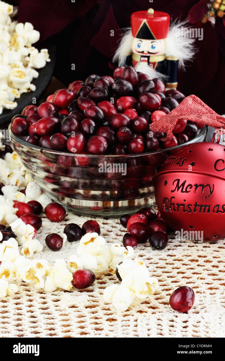 String of popcorn and cranberries with bowl of cranberries, popcorn, gift and ornaments in background. Shallow depth of field. Stock Photo
