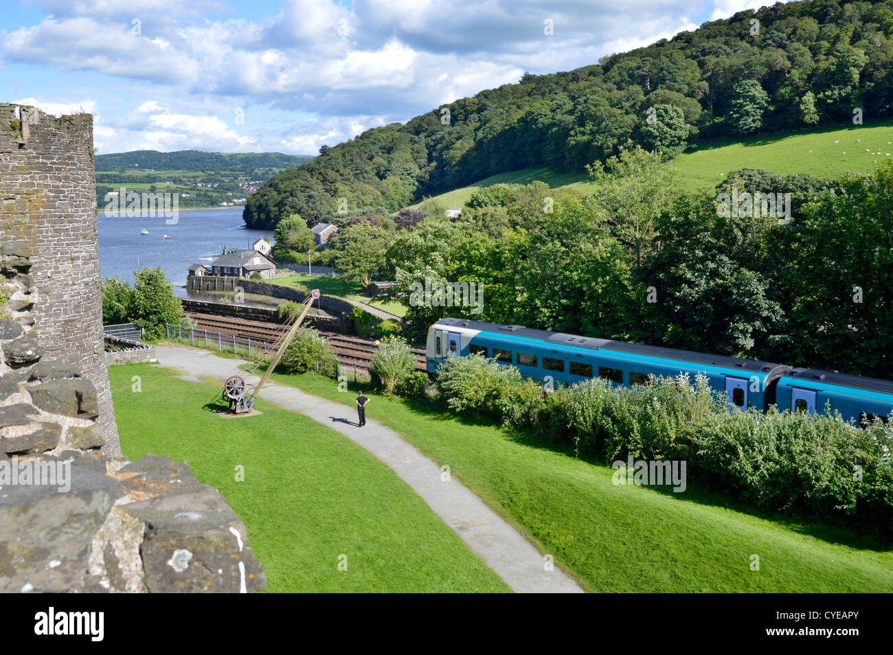 Holyhead to Chester railway line beside historical Conwy castle walls with Arriva train about to cross Stephenson's famous bridge over River Conwy UK Stock Photo