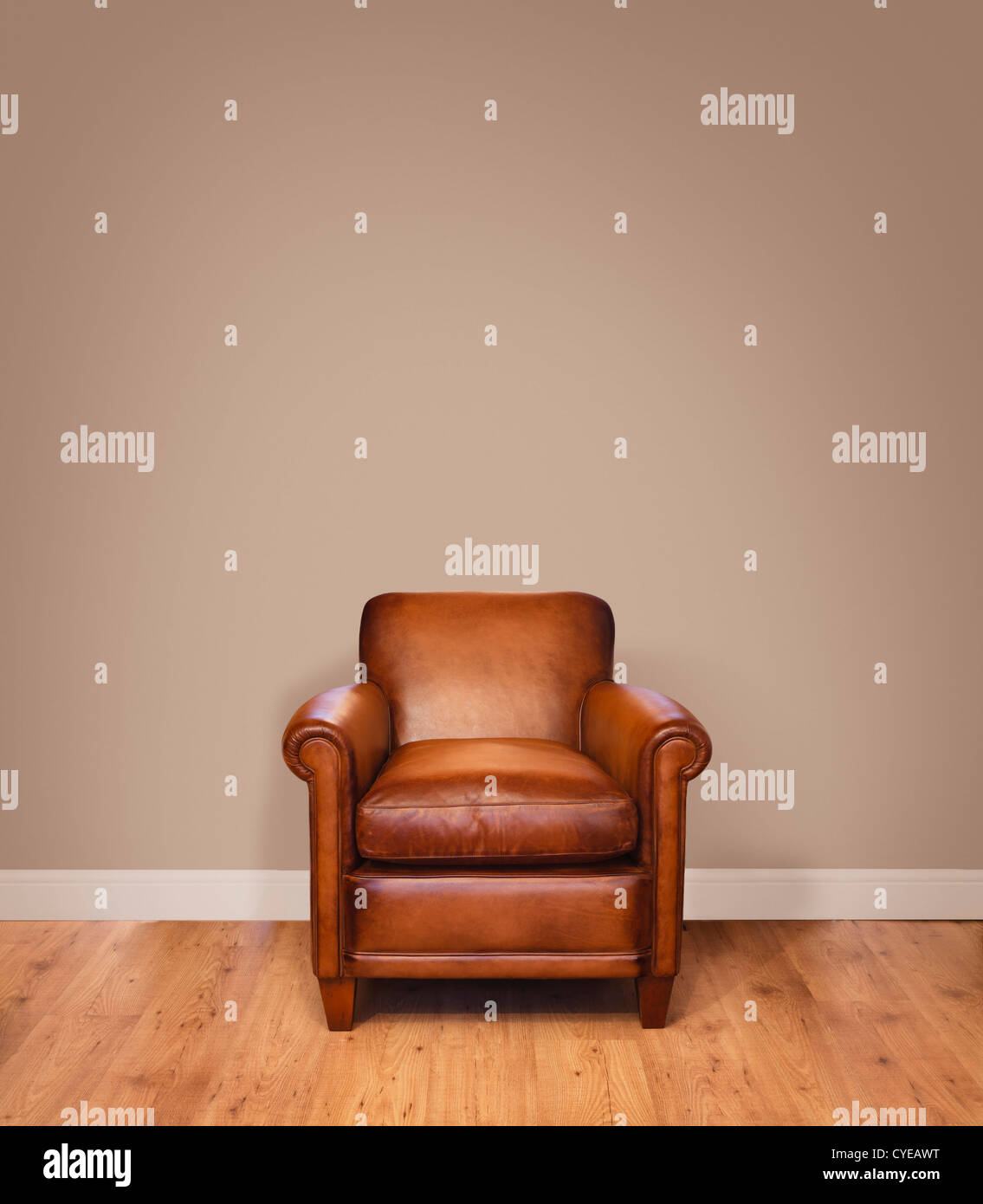 Leather armchair on a wooden floor against a plain background wall with lots of copyspace. The wall has a clipping path. Stock Photo