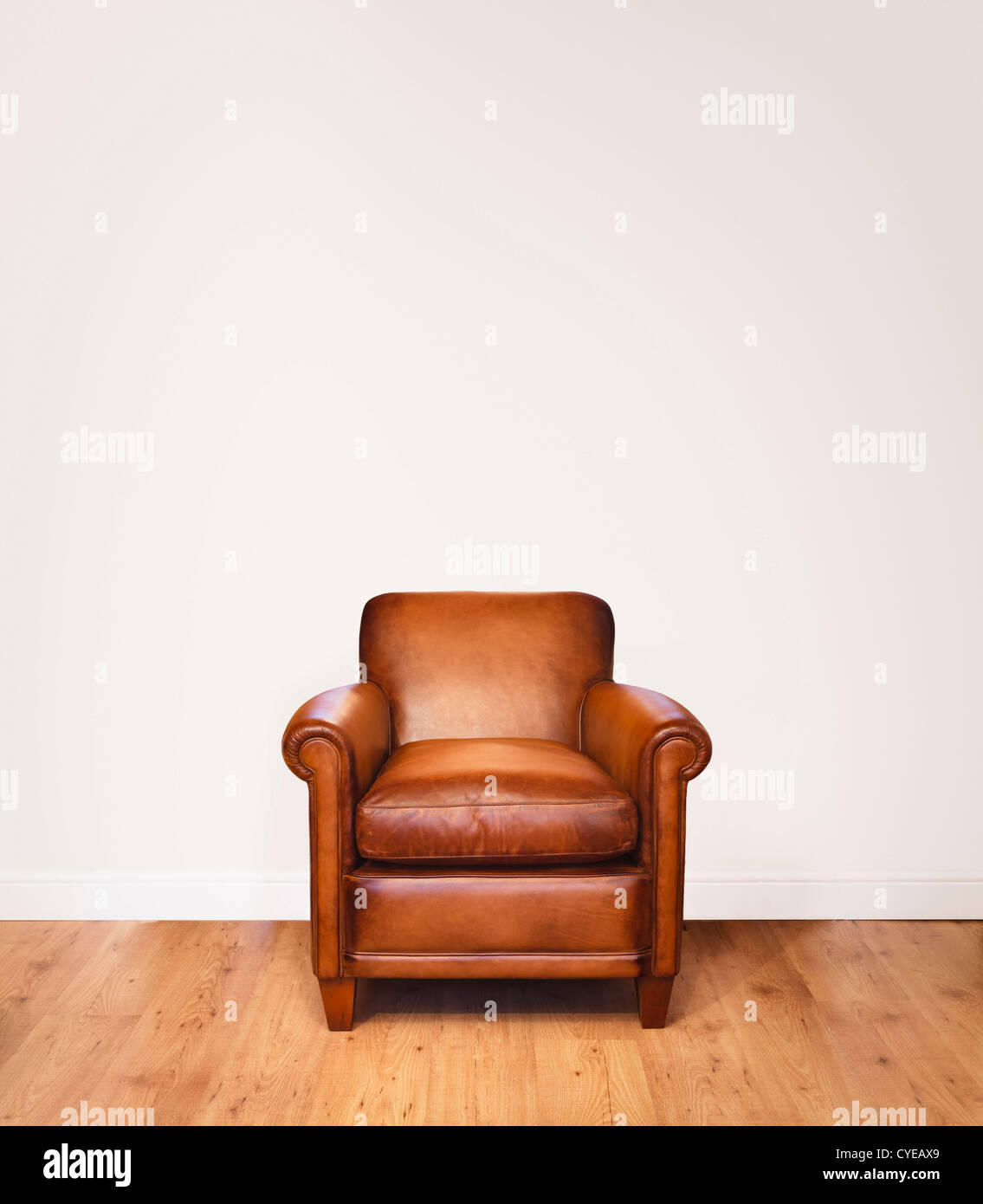 Leather armchair on a wooden floor against a white background with lots of space for copy.  The wall has a clipping path. Stock Photo