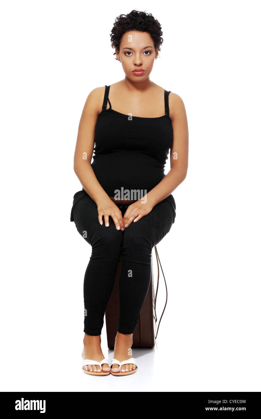 Full length portrait of a sad pregnant woman sitting on a case. Stock Photo