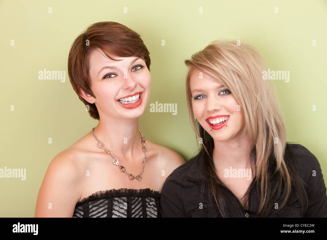 Two young punky looking teens smile in front of a green wall. Stock Photo