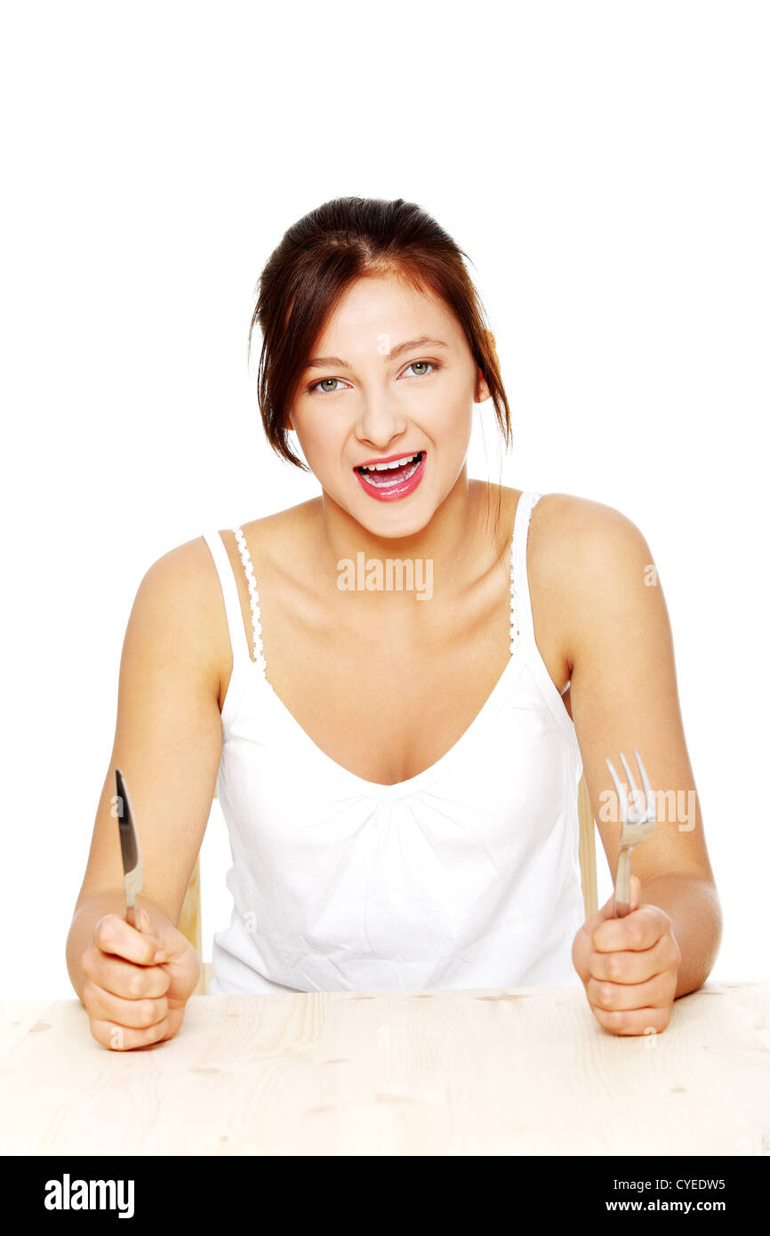 Teen pretty caucasian screaming girl sitting behind the table with fork