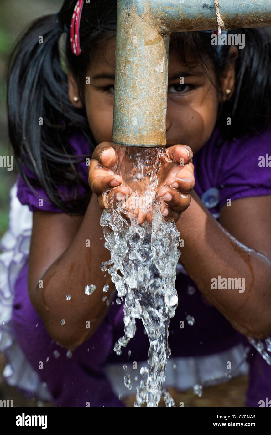 Young Indian girl drinking from a hand water pump in a rural indian village. Andhra Pradesh, India Stock Photo