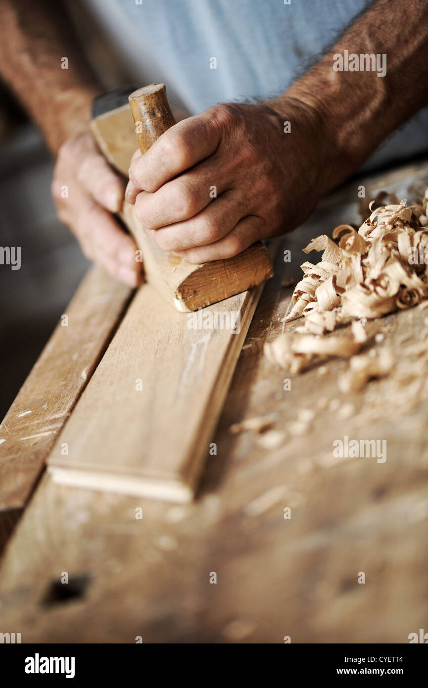 hands of a carpenter planing a plank of wood with a hand plane Stock