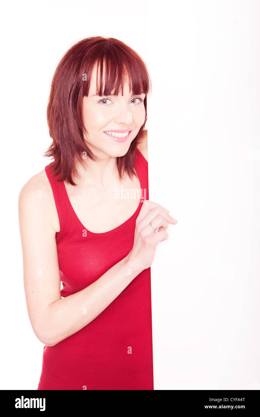 smiling woman in red tank top, her left arm hidden behind a white wood panel Stock Photo