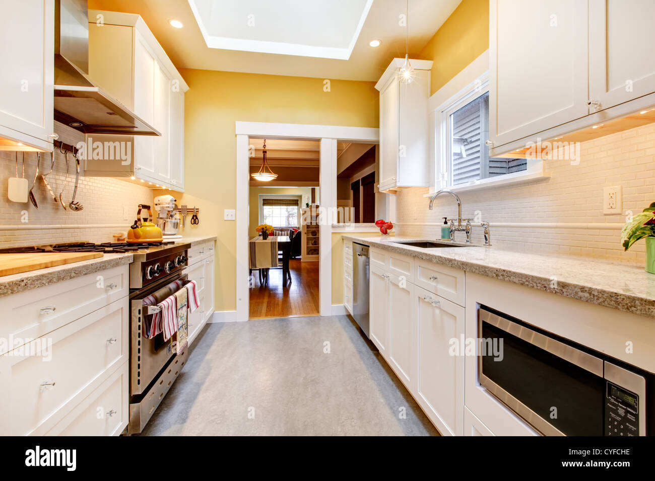 Narrow white and yellow kitchen with skylight and grey floor Stock