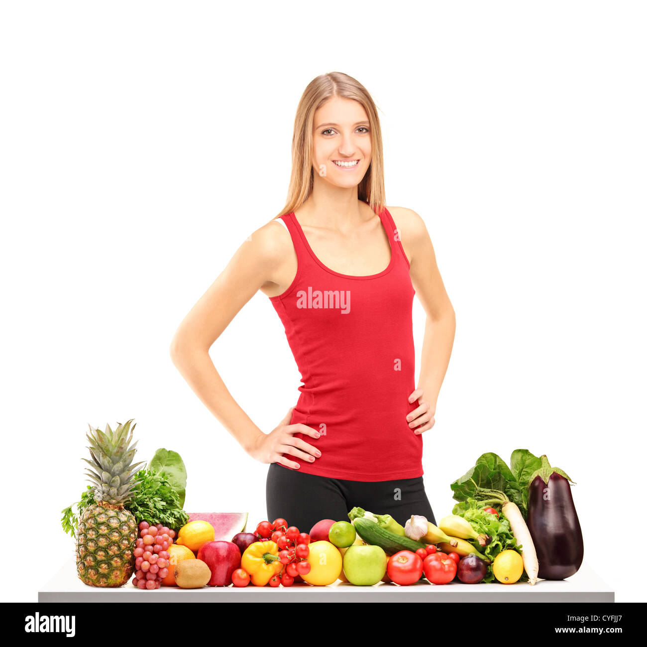 Smiling female athlete posing next to a table with fruits and vegetables isolated on white background Stock Photo