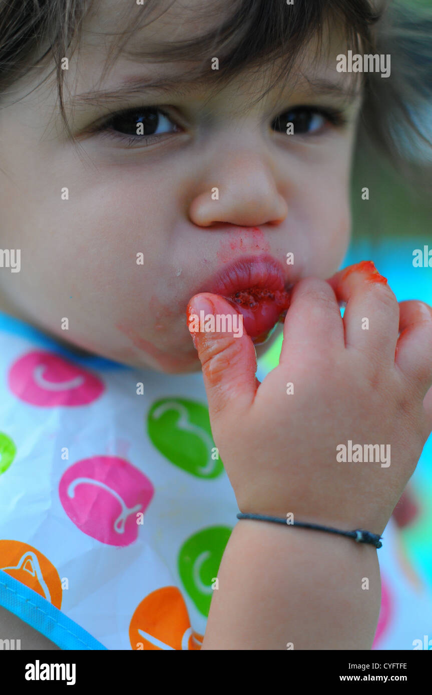 10 month old baby eating a strawberry outdoors in England. Stock Photo