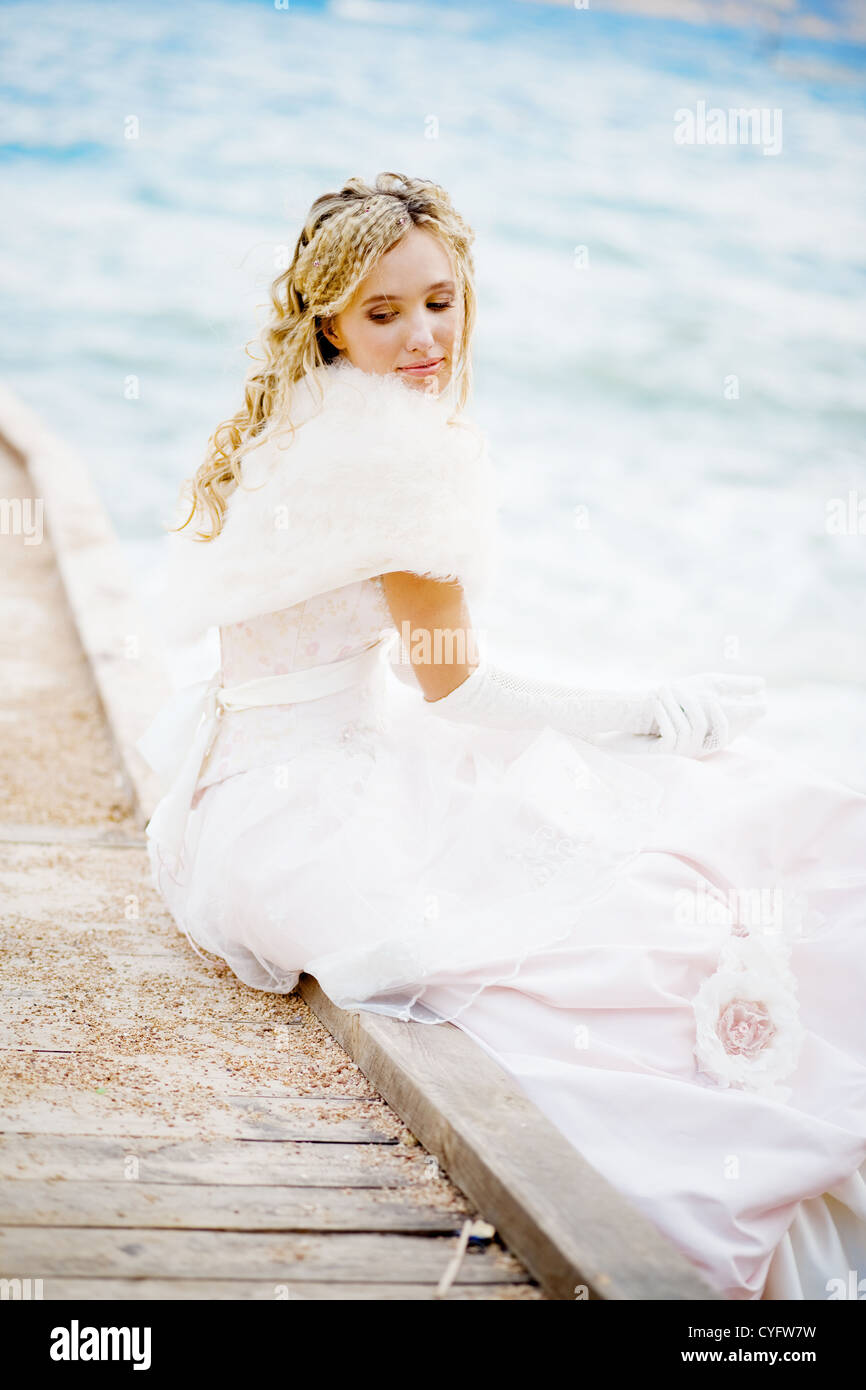 Beautiful happy bride itting on berth at beach and smiling Stock Photo