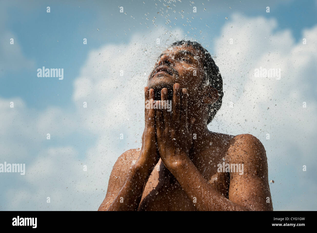 Indian man splashing water on his face against blue sky background. India Stock Photo