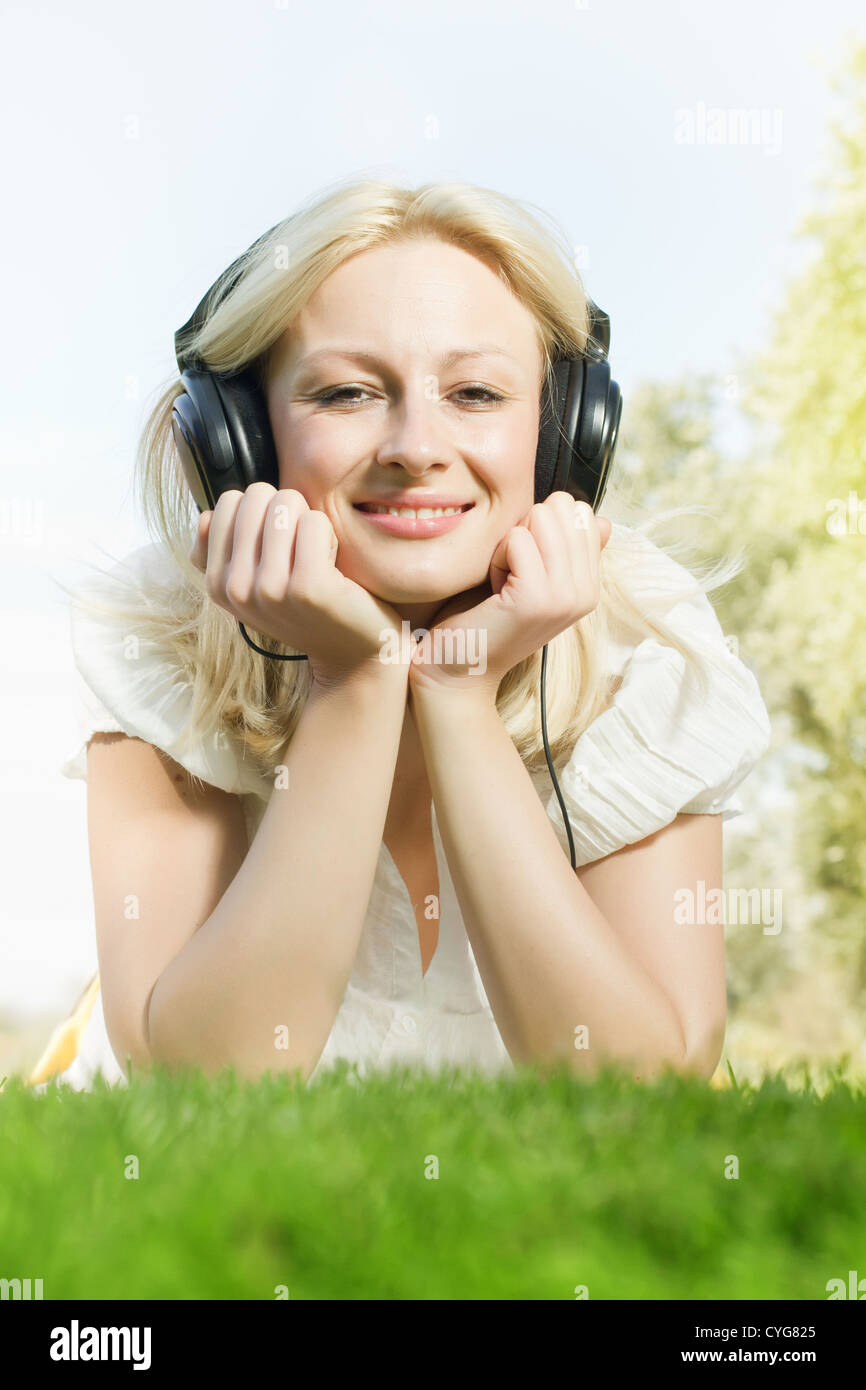 Happiness blonde woman with headphones relaxing on green grass in the ...