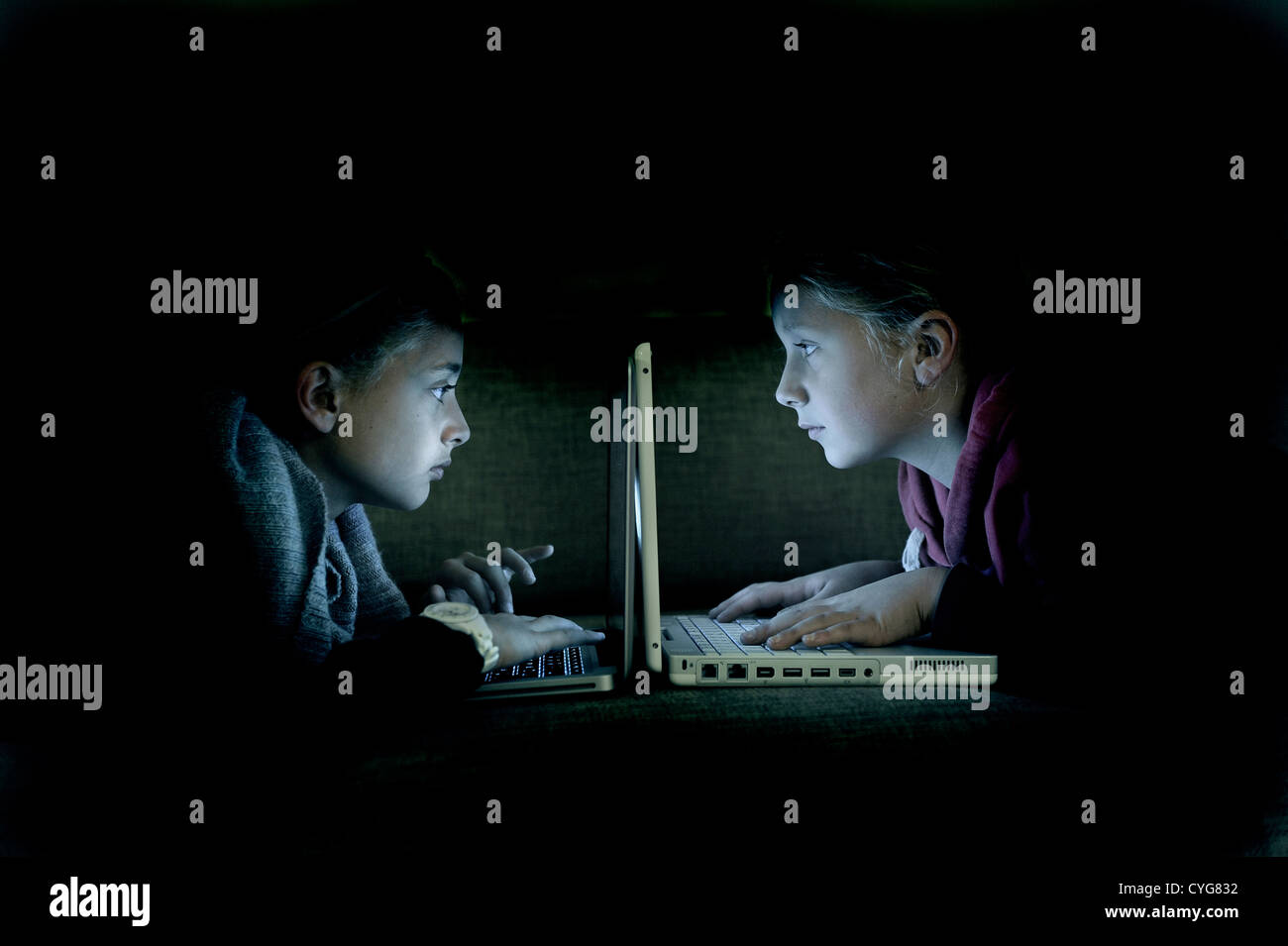 Children playing with computers on the sofa at night. Stock Photo