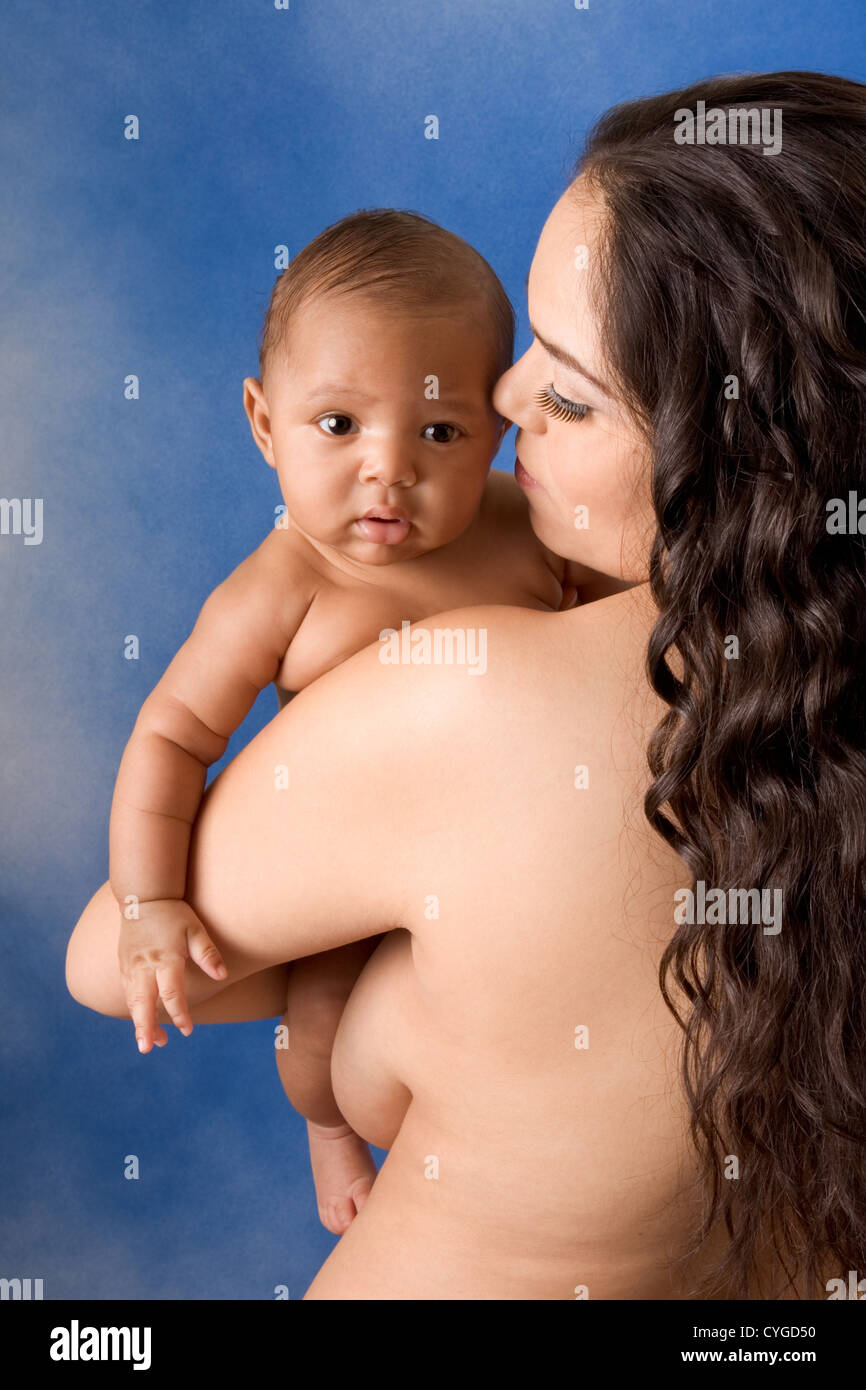 naked Hispanic mom holding her biracial mix of Hispanic and African American baby son against blue background Stock Photo