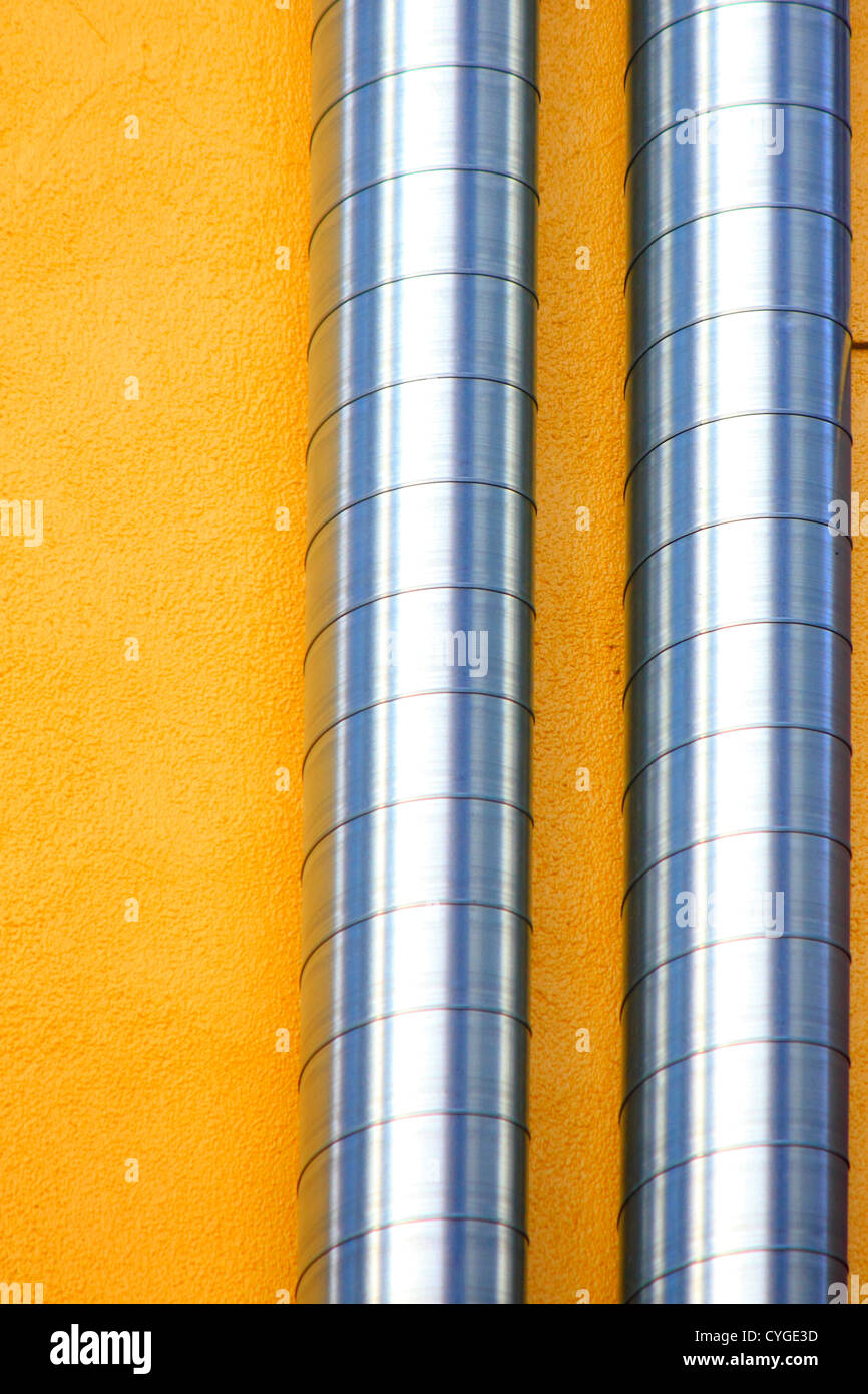 Two ventilation ducts crawling on a yellow wall Stock Photo
