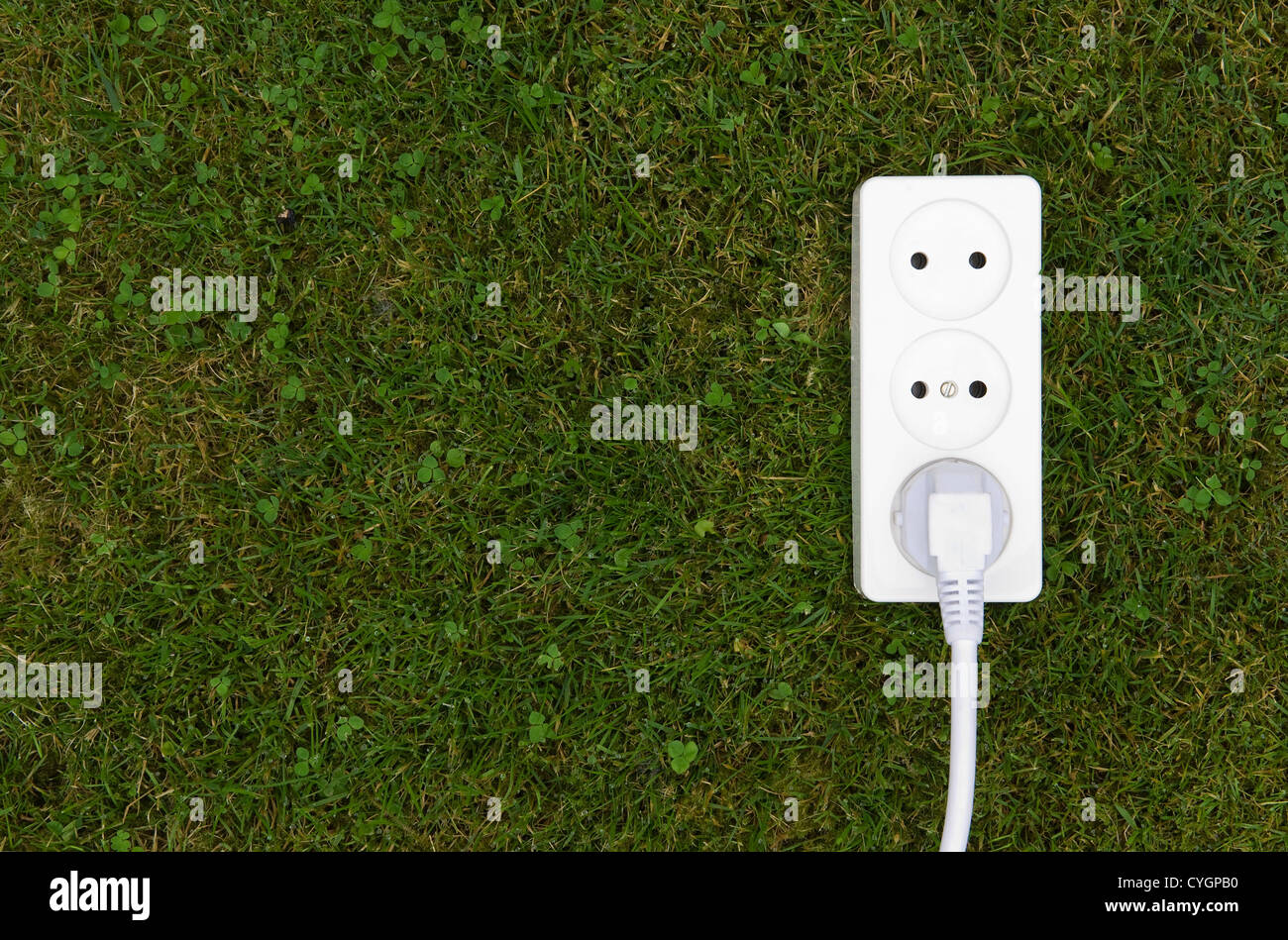 Green energy coming out of an outlet in the grass Stock Photo