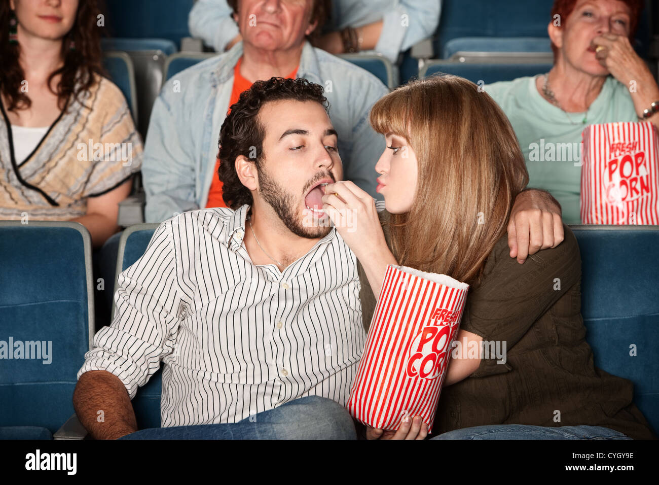 Loving young girlfriend feeds boyfriend popcorn in a theater Stock