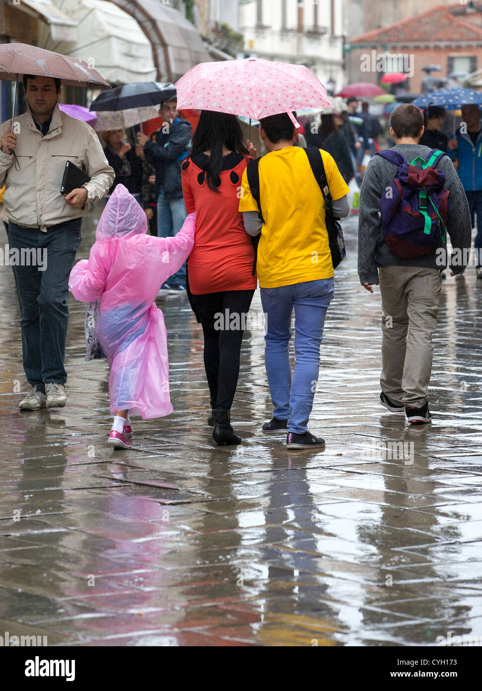 A couple walking in the rain under a pink umbrella with a child in a long pink waterproof cape Stock Photo