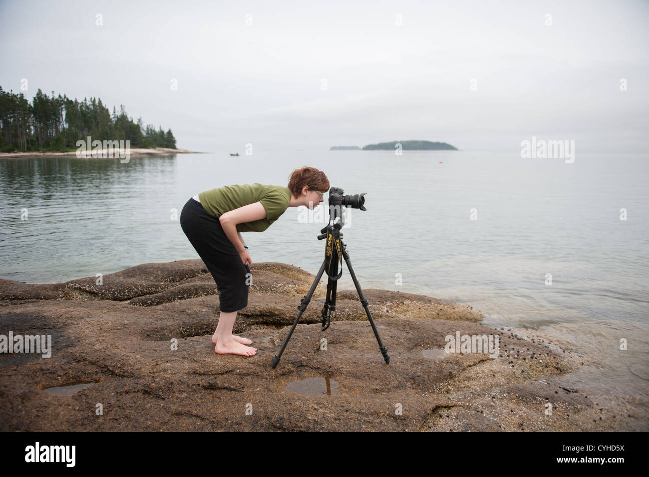 Woman using camera set on tripod and vacationing on coast of Maine Stock Photo