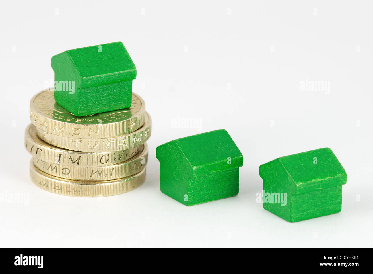 Stack of British pound coins with green wooden houses isolated on a white background Stock Photo